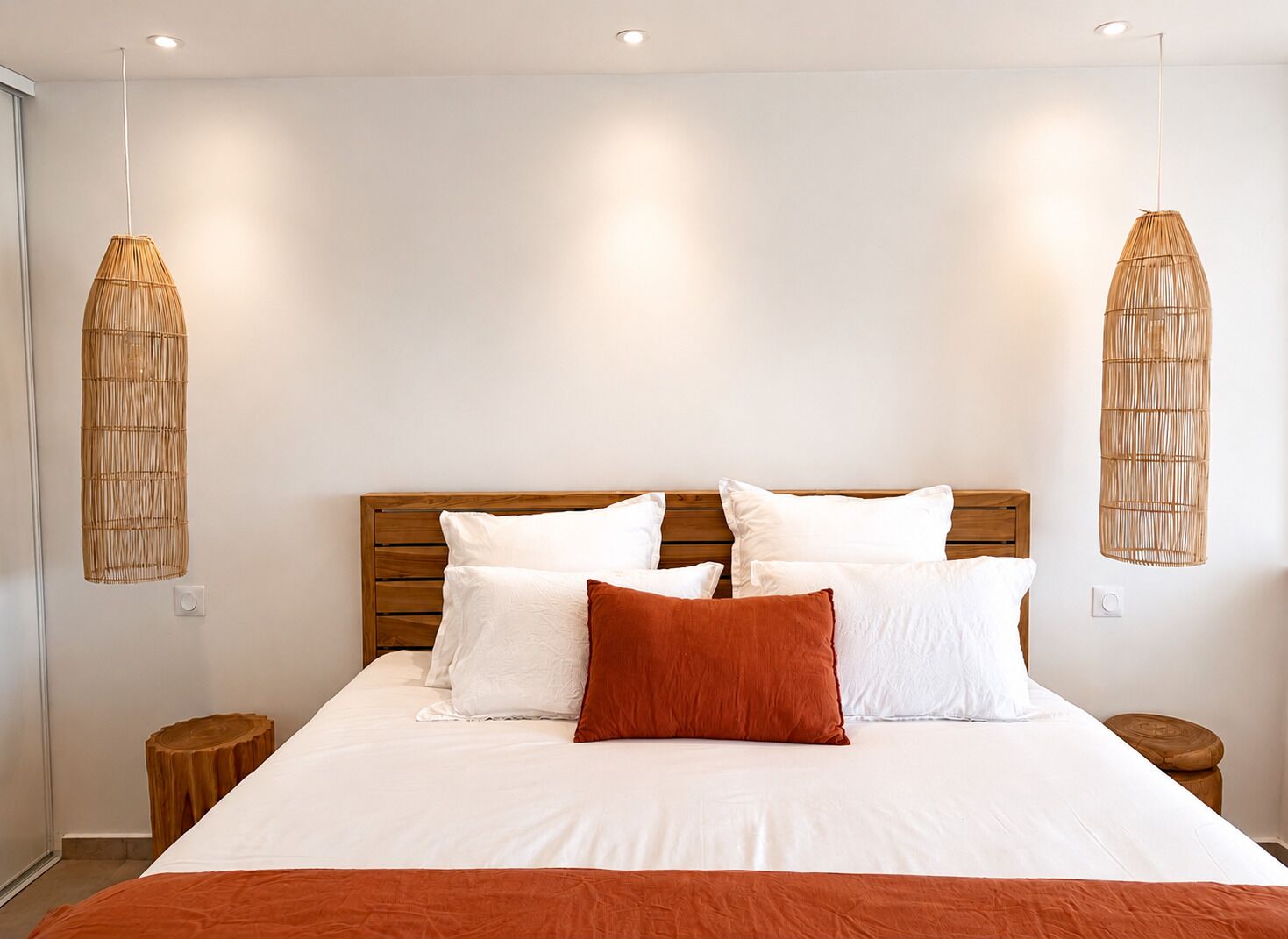 A bedroom with a large bed, two bedside tables, and two hanging lamps.