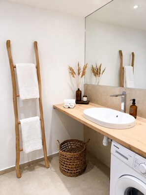 Un baño moderno con un toallero de madera, un lavamanos, un espejo, una lavadora y una cesta de mimbre.