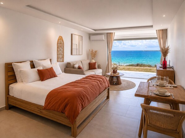 Un dormitorio con una cama grande, un sofá, una mesa de comedor con sillas y vistas al océano.