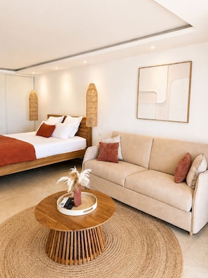 A modern bedroom with a bed, a sofa, a coffee table, and a wall-mounted abstract art piece. - The Ocean Pearl Studio - Ocean View & Beach Access (Orient Bay)
