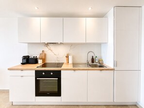 A modern kitchen with white cabinetry, a black induction cooktop, a built-in oven, and a stainless steel sink. - The Ocean Pearl Studio - Ocean View & Beach Access (Orient Bay)