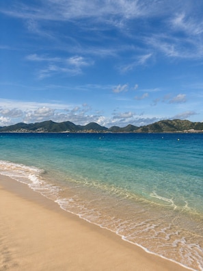 A beach with clear water, a sandy shore, and distant mountains under a blue sky. - The Ocean Pearl Studio - Ocean View & Beach Access (Orient Bay)