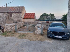 A stone house with a red-tiled roof, a gated entrance, and a parked car. - Peaceful Two Bedroom Stone House in the Heart of Vis Island  (Podhumlje)