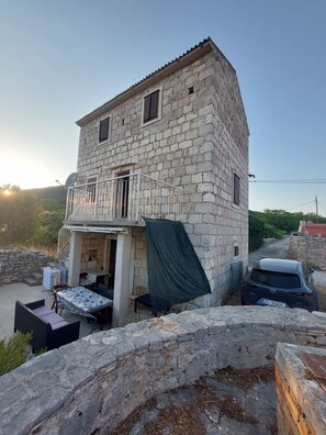 Un edificio in pietra con un balcone, un'auto parcheggiata di fronte e un muro di pietra in primo piano.