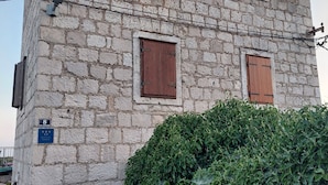 A stone building with three windows, each with wooden shutters, and an air conditioning unit mounted on the wall.