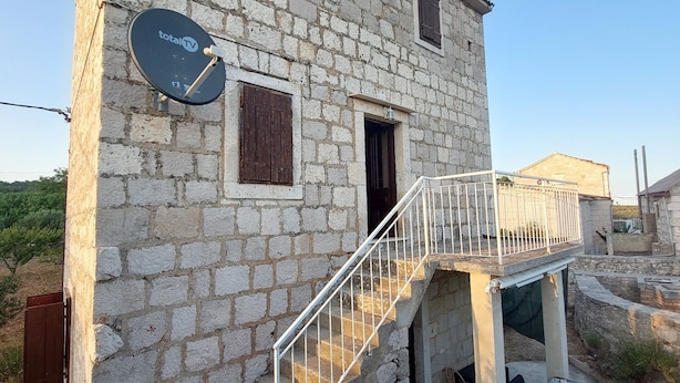 A stone building with a satellite dish, a staircase, and outdoor furniture.