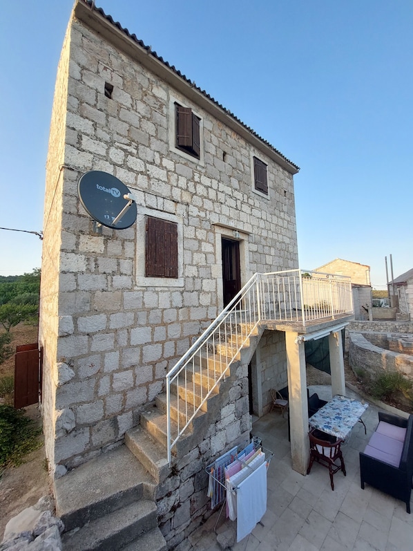 A stone building with a satellite dish, a staircase, and outdoor furniture.