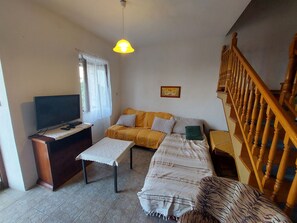 Un salon comprenant une télévision, un canapé, une table basse, un escalier et un luminaire au plafond.