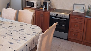 A compact kitchen with a refrigerator, microwave, toaster, and oven. There is a dining table with chairs and a patterned tablecloth.