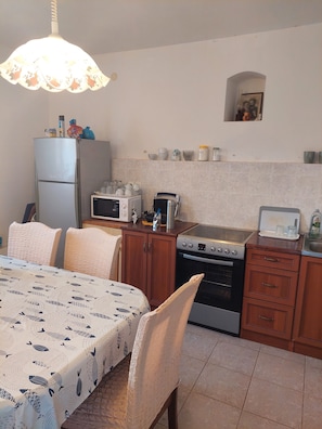 A compact kitchen with a refrigerator, microwave, toaster, and oven. There is a dining table with chairs and a patterned tablecloth.