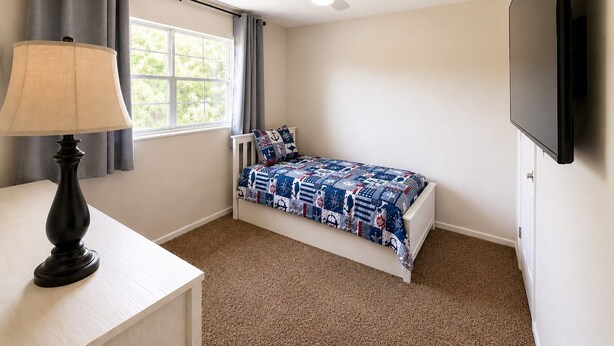 Een slaapkamer met een enkel bed, een bureau, een lamp, een plafondventilator en een televisie.
