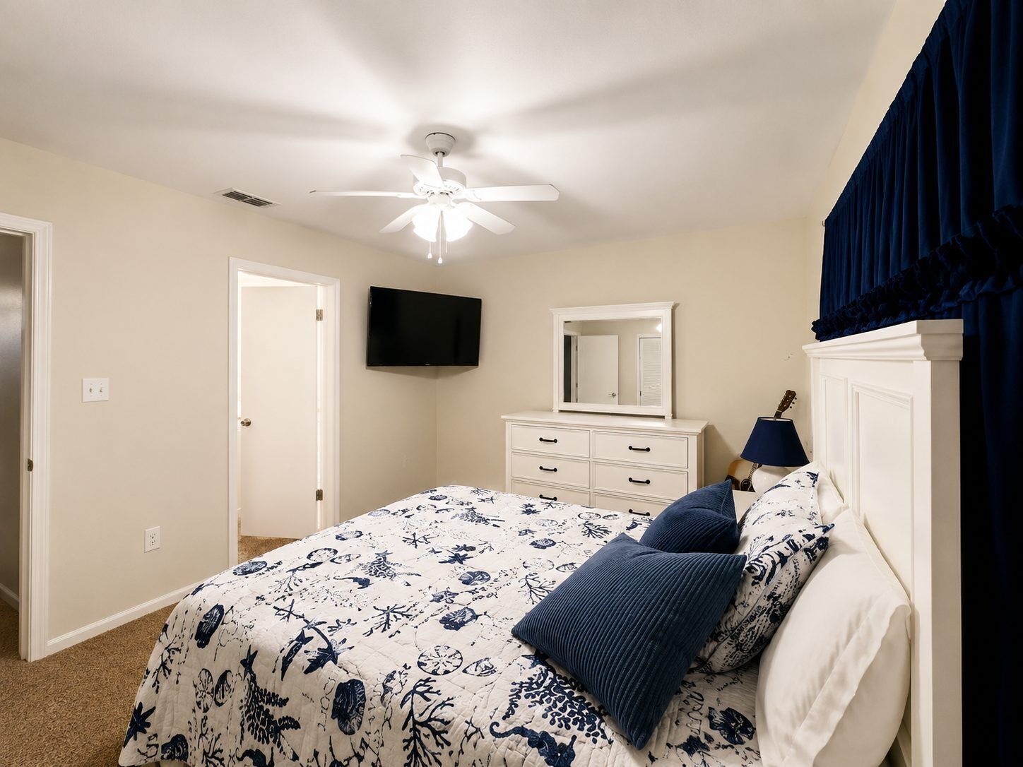 A bedroom with a bed, a ceiling fan, a television, a dresser, and a lamp.