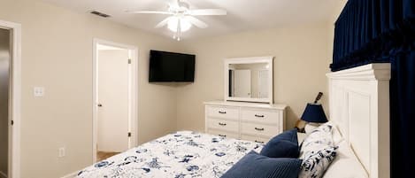 A bedroom with a bed, a ceiling fan, a television, a dresser, and a lamp.