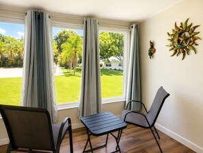 Ein Zimmer mit Blick auf eine grüne Wiese und Bäume, mit zwei Stühlen, einem kleinen Tisch und einem Wanddekor.
