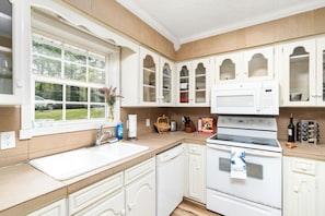 A kitchen with white cabinets, a microwave, an oven, a sink, and a window with a view of a car and trees. - Charming 3-bedroom townhome - Hot Springs Village - Convenient, near West Gate (Hot Springs)