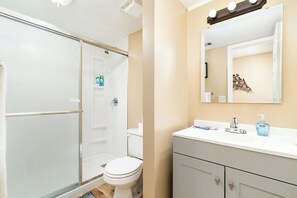 A bathroom with a glass-enclosed shower, a toilet, a sink with a mirror, and toiletries. - Charming 3-bedroom townhome - Hot Springs Village - Convenient, near West Gate (Hot Springs)