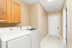 A laundry room with a front-loading washer and dryer, wooden cabinets above, and a white door in the background. - Charming 3-bedroom townhome - Hot Springs Village - Convenient, near West Gate (Hot Springs)