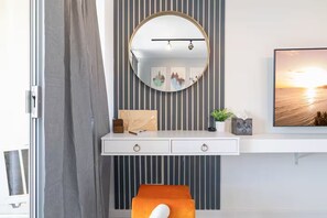 Ein modernes Zimmer mit weißem Schreibtisch, einem runden Spiegel, einem gerahmten Bild und einem Fenster mit Sonnenuntergangsblick.