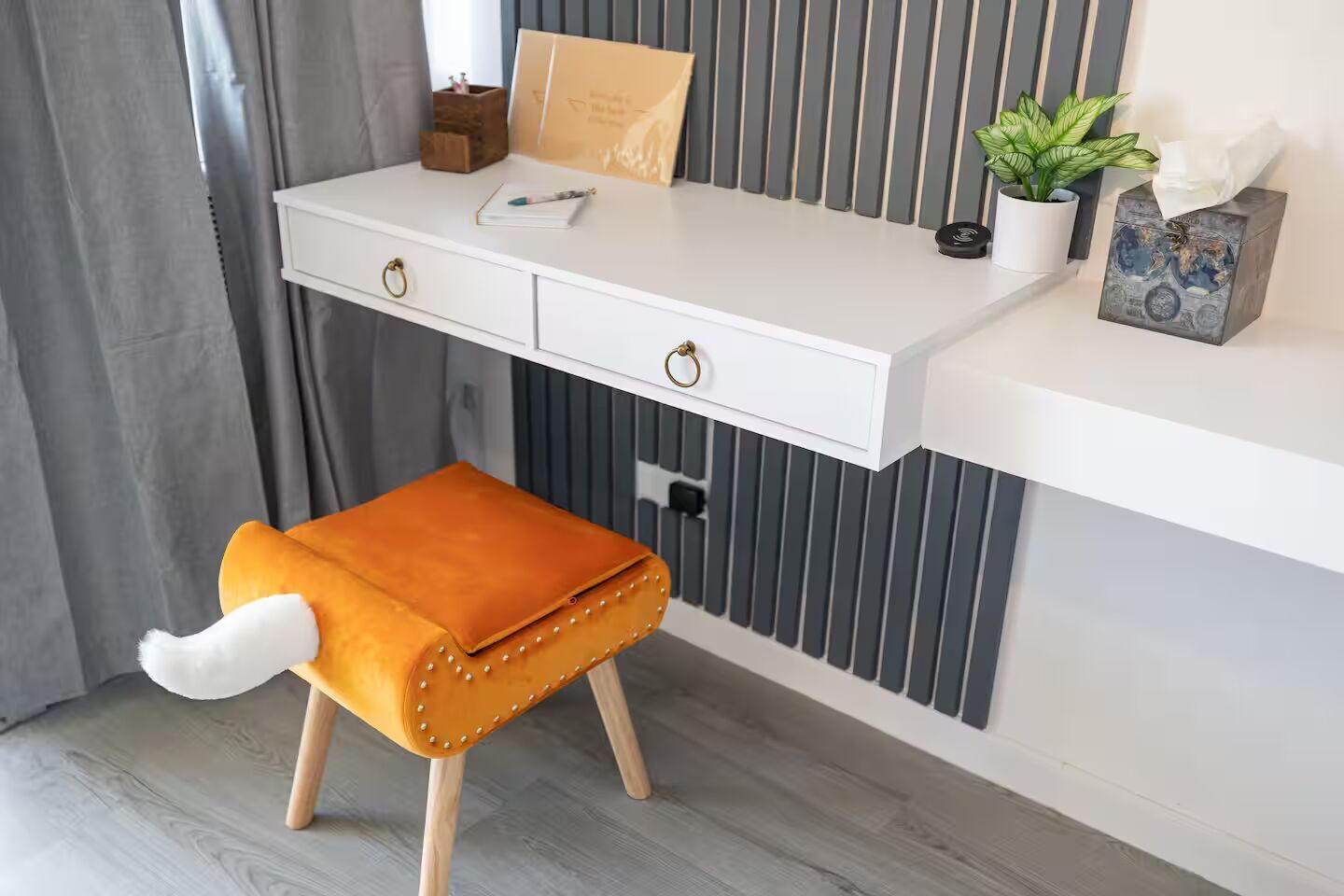 Un escritorio blanco con dos cajones, una pequeña planta en maceta y un estuche decorativo.