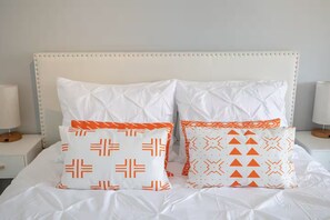 Ein Bett mit weißer Bettwäsche und zwei Zierkissen mit geometrischen Mustern.