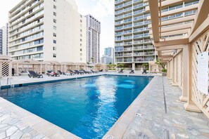 Ein Pool mit Liegestühlen und einer überdachten Liegefläche, umgeben von Hochhäusern.