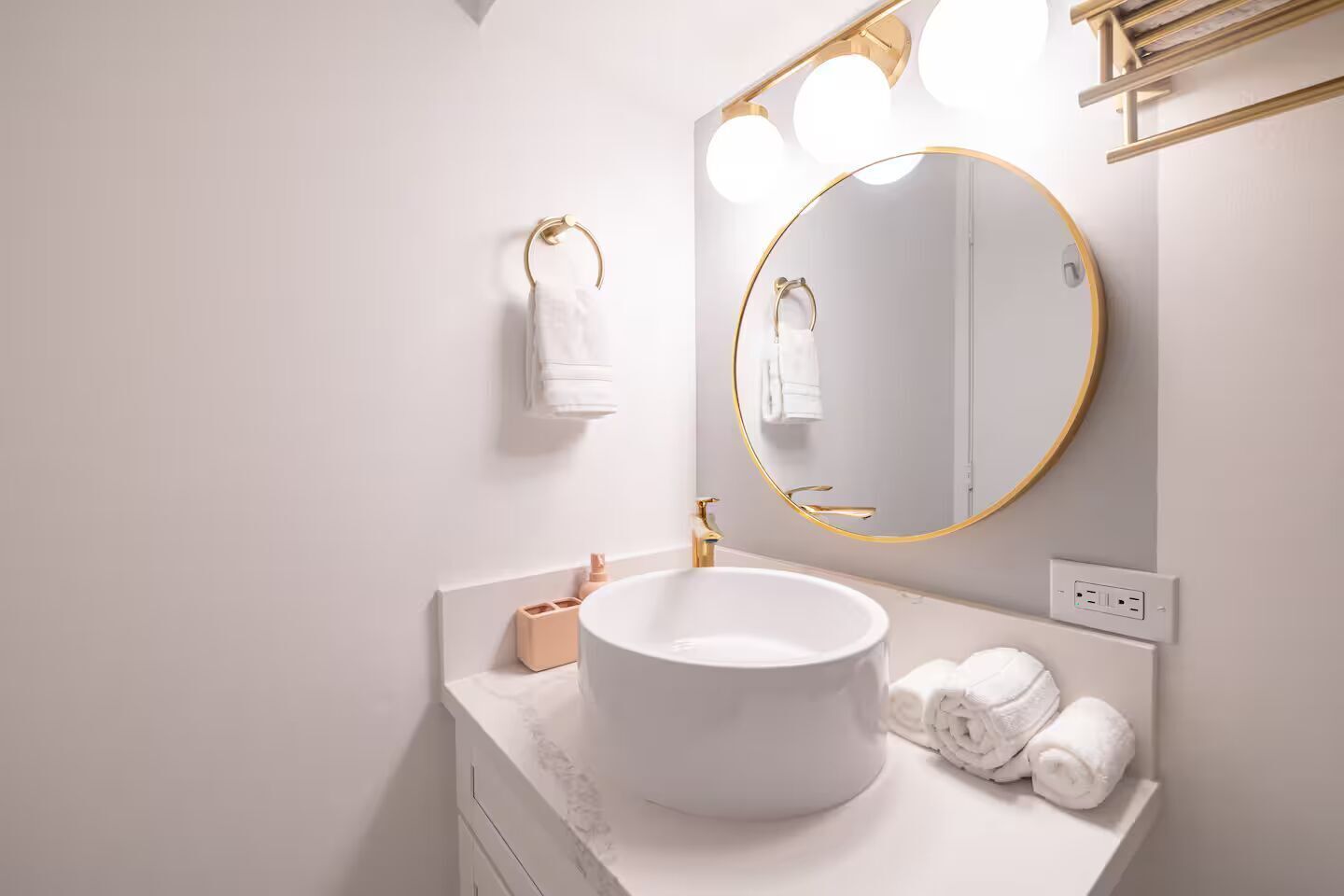 Un bany modern amb un mirall rodó, un lavabo blanc i detalls daurats.