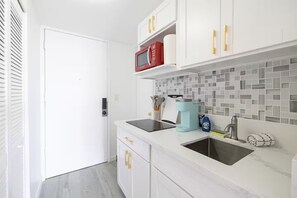 Eine moderne Küche mit weißen Schränken, einer Mikrowelle, einer Kaffeemaschine und einer gefliesten Spritzschutzwand.