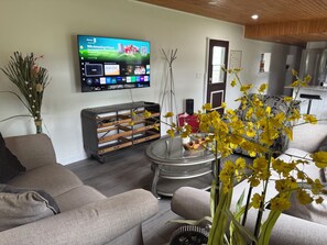 A living room with a flat-screen TV mounted on the wall, a sofa, a coffee table, and a decorative vase with yellow flowers.