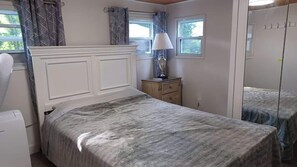 A bedroom with a bed, a nightstand, a lamp, a window, and a mirror.