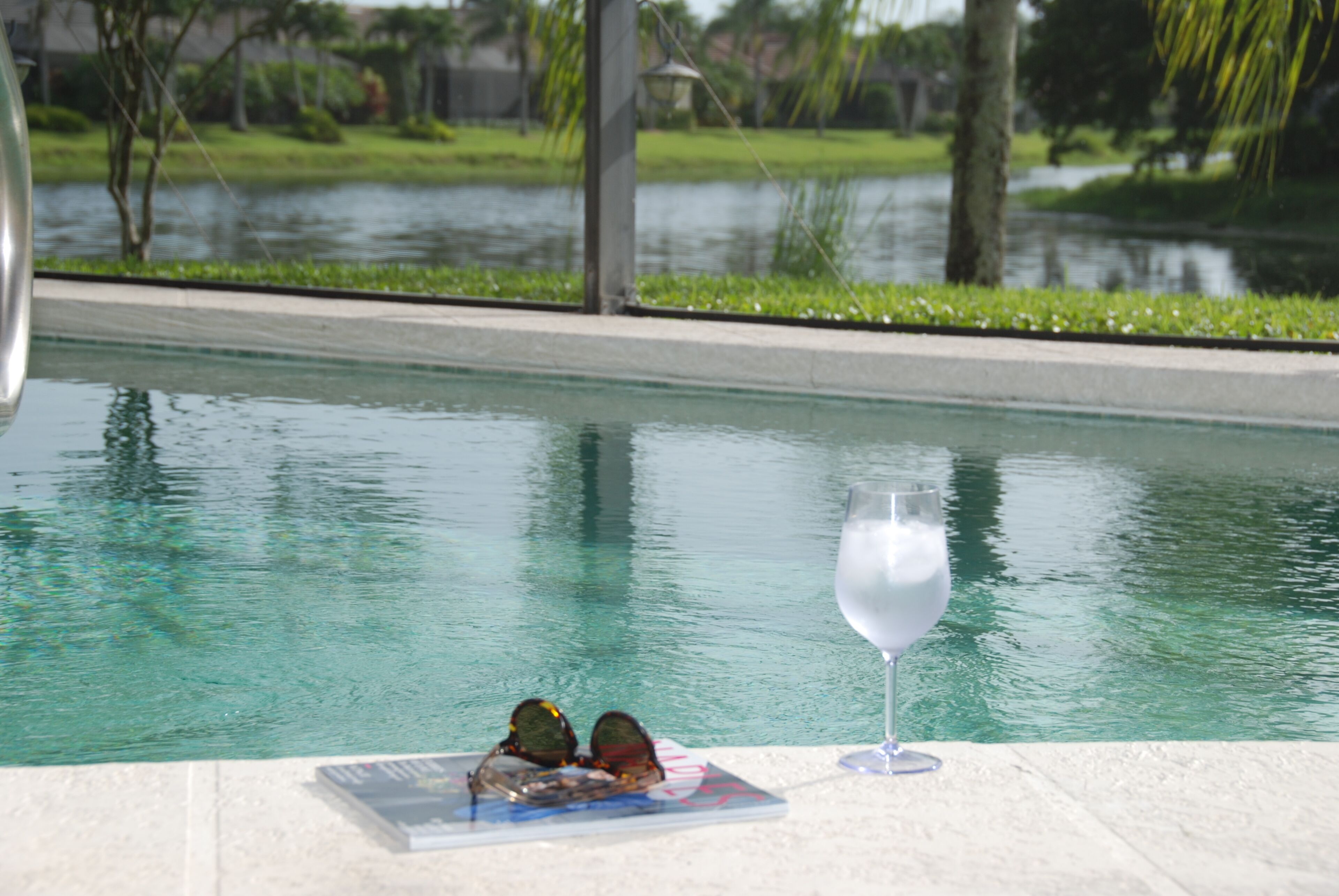 A swimming pool with a glass of water and sunglasses on the edge.
