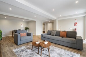 A modern living room with grey sofas, a coffee table, and a rug. - Oceanea Apartment by Homie (Santa Cruz)