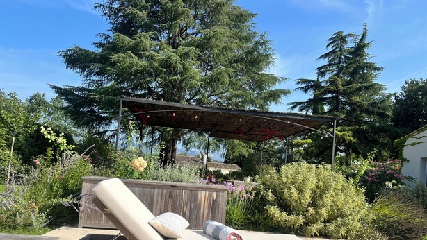 A sun lounger with a wooden bench and a pergola overhead.