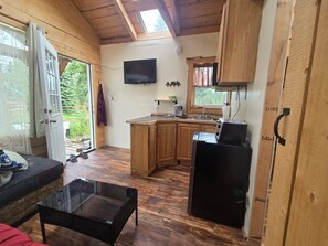 Eine kompakte Küche mit Holzschränken, einem schwarzen Kühlschrank, einer Kaffeemaschine und einem Fernseher an der Wand.