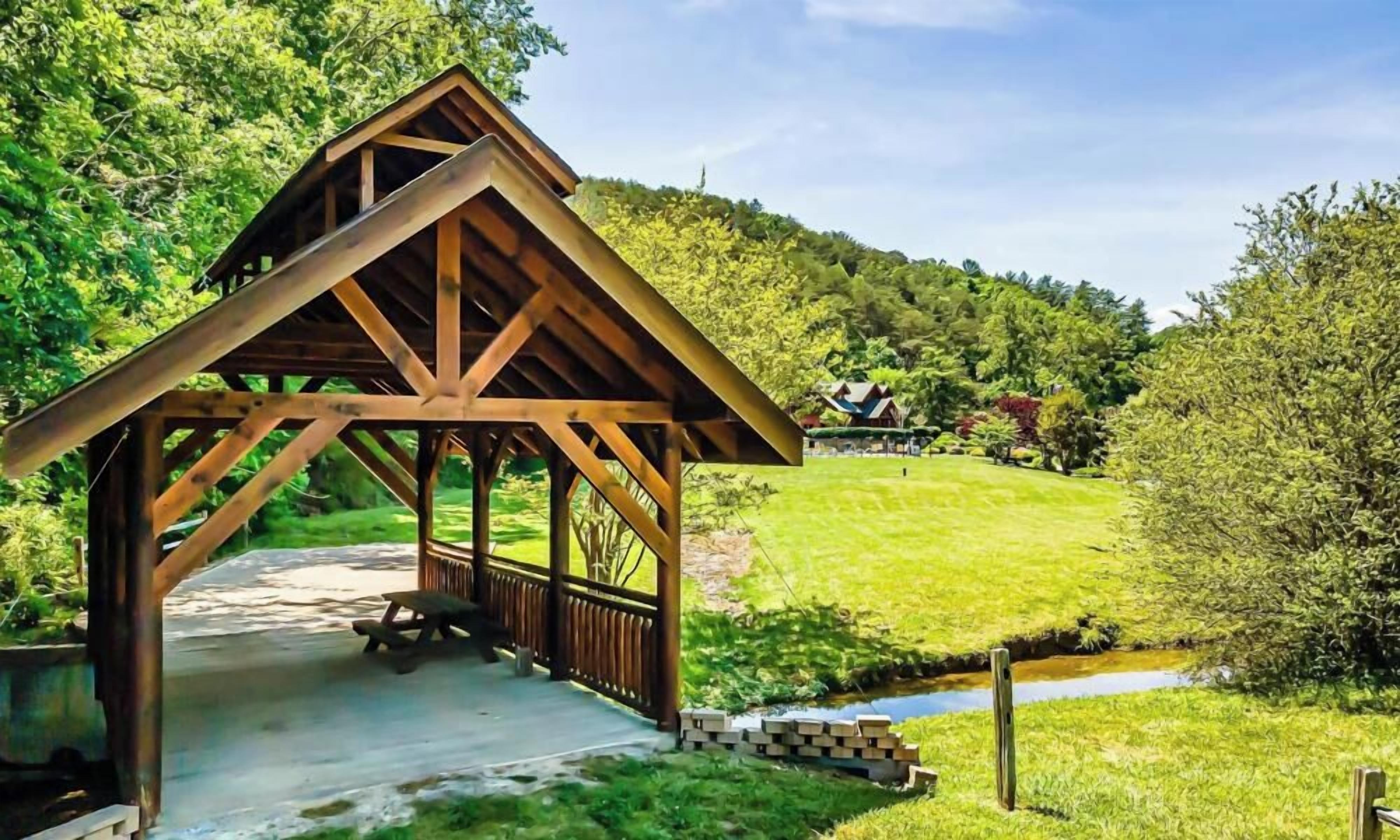 Un pavillon en bois avec un banc, entouré d’une végétation luxuriante et traversé par un petit ruisseau.