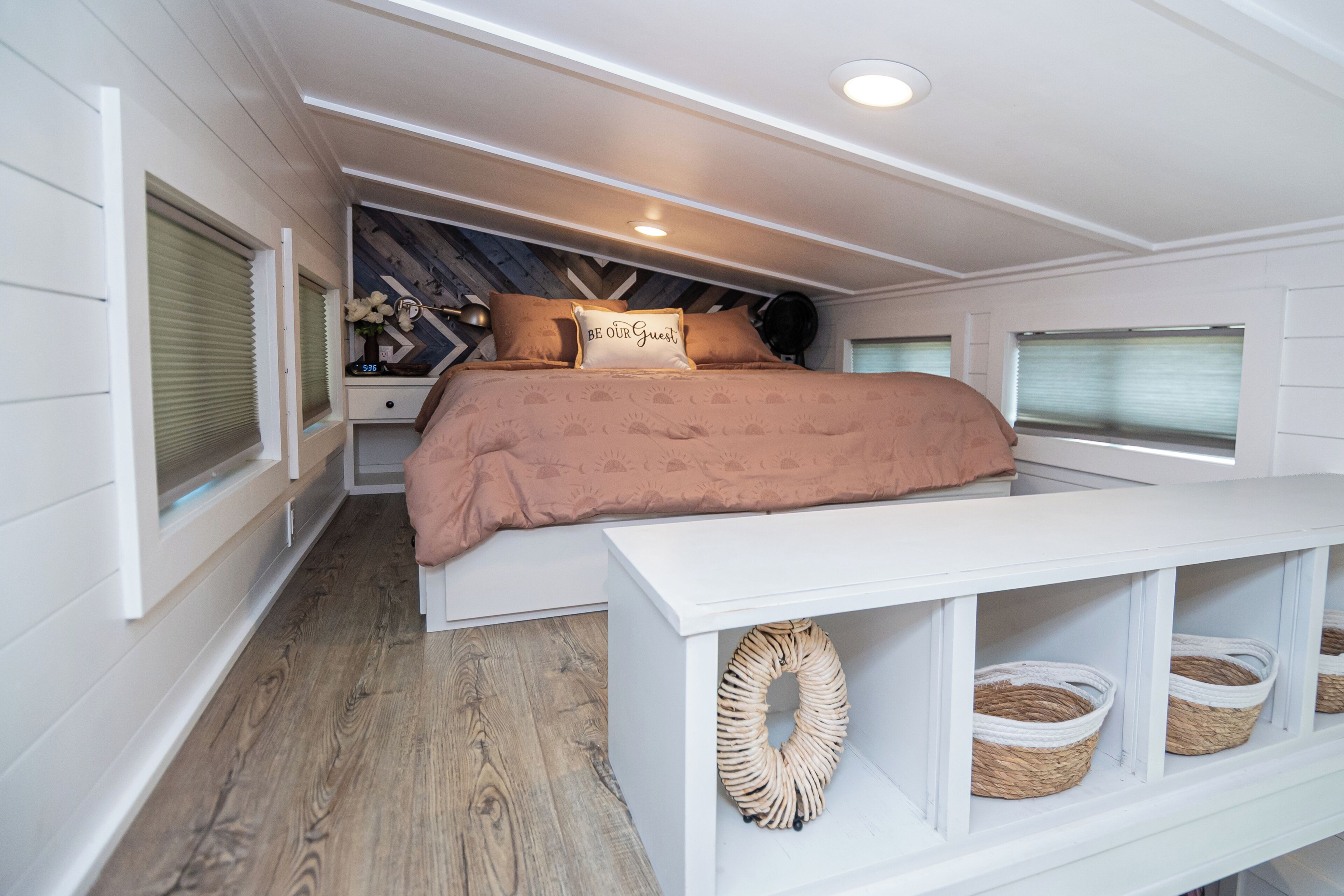A bedroom with a bed, bedside tables, and a white bench with baskets.