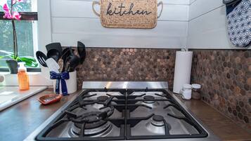 A kitchen with a gas stove, a woven kitchen sign, and a hexagonal tile backsplash.