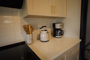 Eine Küche mit weißen Schränken, einer Kaffeemaschine und einem Wasserkocher auf der Arbeitsfläche.