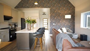 Uma cozinha moderna com ilha central, banquetas, um sofá e papel de parede estampado.