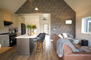 A modern kitchen with a central island, bar stools, a sofa, and a patterned wallpaper. - Modern Luxury Cabin, Fireplaces, Hot Tub Paducah (West Paducah)