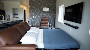 Quarto de hotel com cama, sofá, televisão, espelho e banheiro.