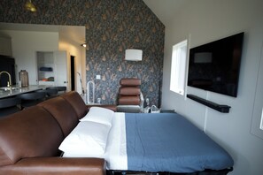 A hotel room with a bed, a sofa, a TV, a mirror, and a bathroom. - Modern Luxury Cabin, Fireplaces, Hot Tub Paducah (West Paducah)