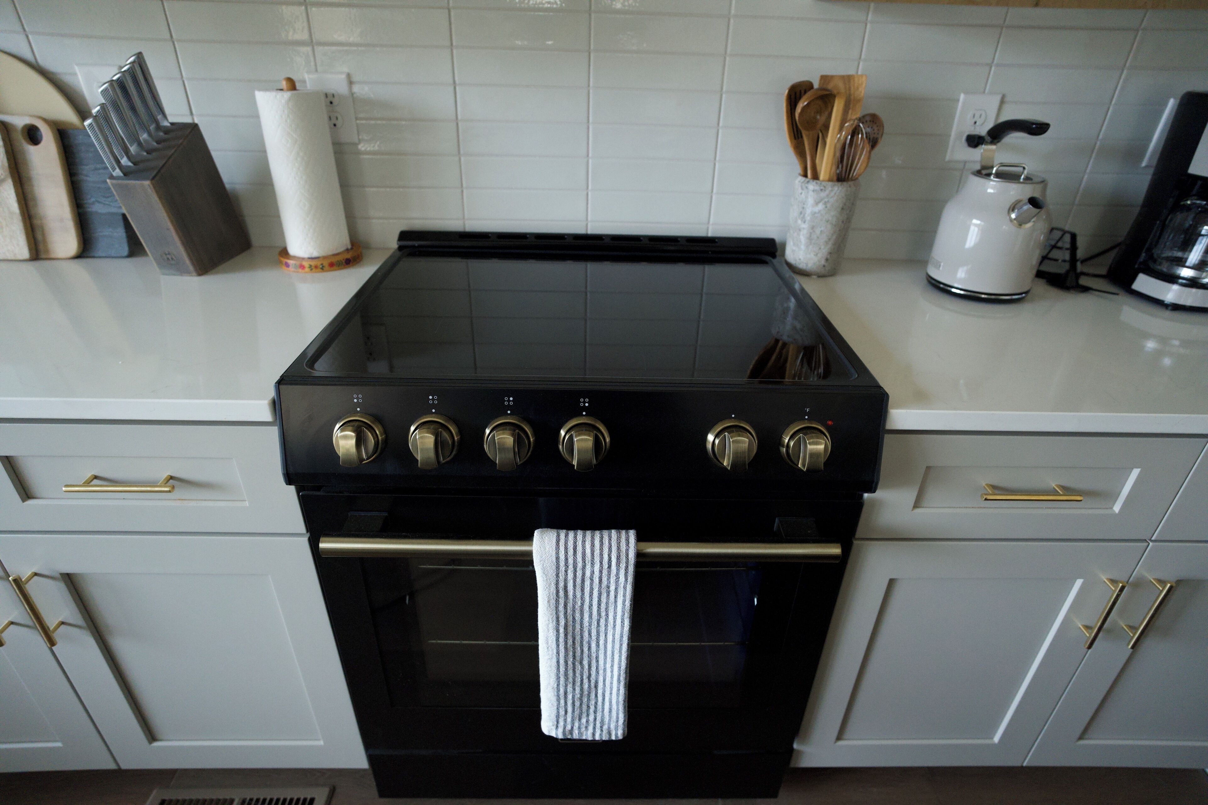 Una cucina con un piano cottura nero, pensili bianchi e un bollitore in acciaio inossidabile.
