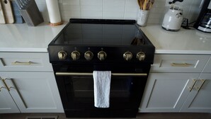 Uma cozinha com fogão preto, armários brancos e chaleira de aço inoxidável.