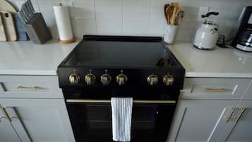 Una cucina con un piano cottura nero, pensili bianchi e un bollitore in acciaio inossidabile.