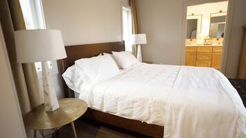 Une chambre d’hôtel avec un lit, deux lampes de chevet, une table ronde et une salle de bain visible à travers une porte ouverte.