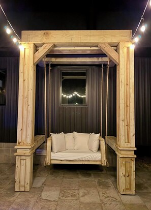 Un columpio de madera con asiento acolchado y cuerdas, sostenido por una estructura de madera, sobre un fondo oscuro.
