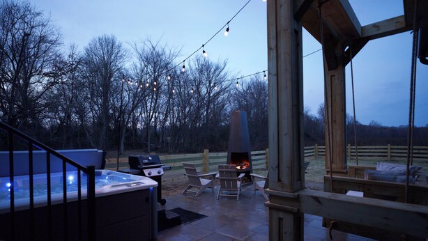 Um pátio externo com banheira de hidromassagem, churrasqueira e lareira.