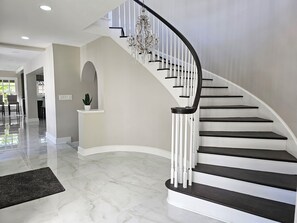 Eine geschwungene Treppe mit weißen Geländern und dunklen Stufen, die zu einer oberen Etage führt.