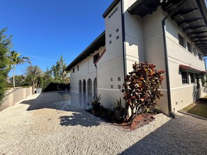 A building with a white facade, multiple windows, and a covered outdoor area with gravel. - Lovely 4-bedroom house with AC in beautiful Tampa (Tampa)