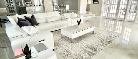 A modern living room with a white sofa, coffee table, and a dining area with chairs.
